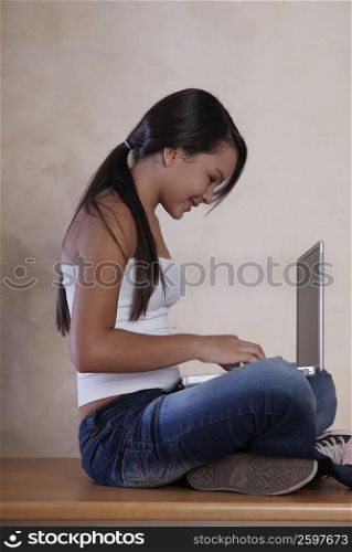 Side profile of a teenage girl sitting on the floor and using a laptop