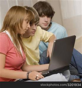 Side profile of a teenage girl using a laptop with her friends sitting beside her