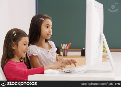 Side profile of a two schoolgirls using a computer in a classroom