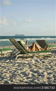 Side profile of a woman reclining on a lounge chair on the beach