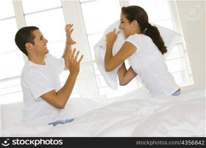 Side profile of a young couple having a pillow fight on the bed