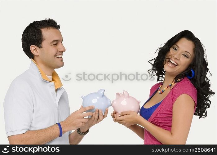 Side profile of a young couple holding piggy banks and smiling