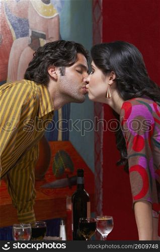 Side profile of a young couple kissing each other in a restaurant