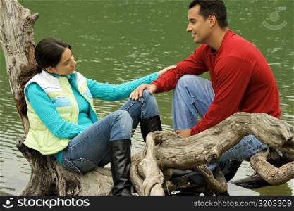 Side profile of a young couple sitting on a tree over a lake