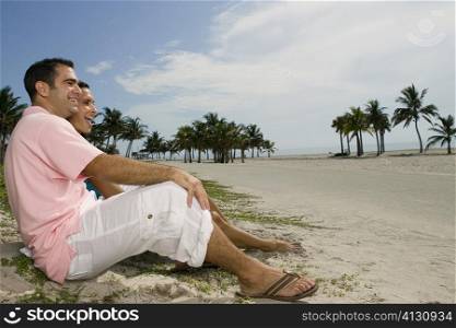 Side profile of a young couple smiling and sitting together on the beach