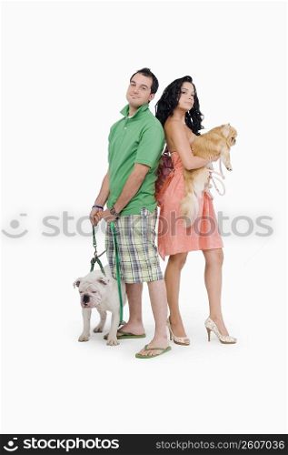 Side profile of a young couple standing back to back with their dogs