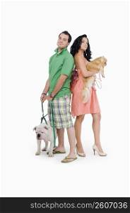 Side profile of a young couple standing back to back with their dogs
