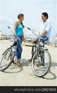 Side profile of a young couple standing on the beach with their bicycles