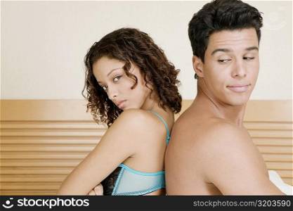 Side profile of a young man and a teenage girl sitting back to back on the bed