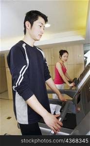 Side profile of a young man and a young woman exercising in a gym