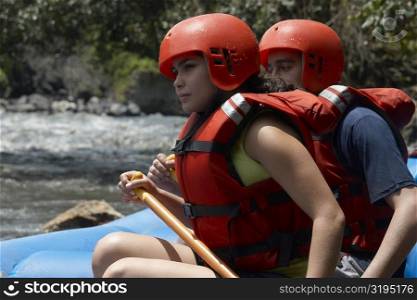 Side profile of a young man and a young woman rafting in a river