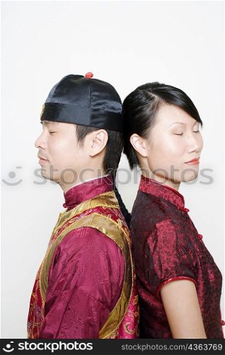 Side profile of a young man and a young woman standing back to back with their eyes closed