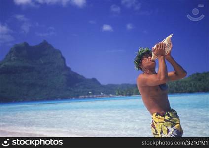 Side profile of a young man blowing a conch shell on the beach, Hawaii, USA