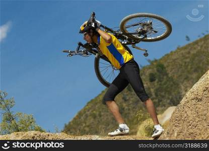 Side profile of a young man carrying a mountain bike on his shoulders