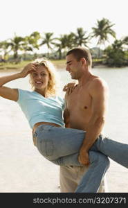 Side profile of a young man carrying a young woman on the beach