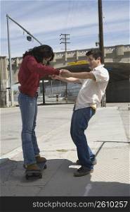 Side profile of a young man helping a young woman in skateboarding