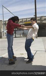 Side profile of a young man helping a young woman in skateboarding