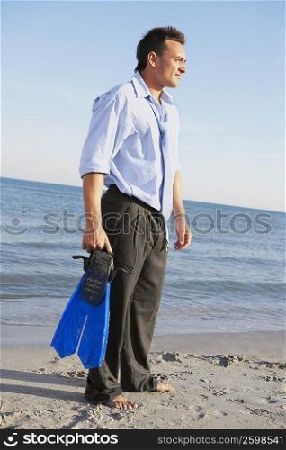 Side profile of a young man holding flipper and standing on the beach