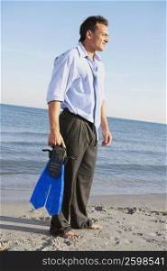 Side profile of a young man holding flipper and standing on the beach