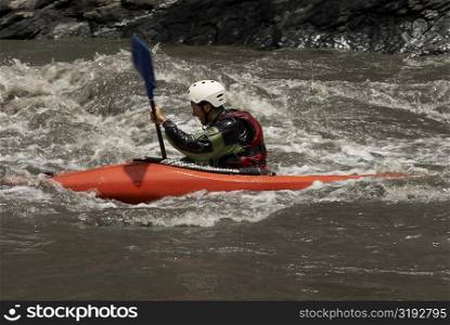 Side profile of a young man kayaking in a river