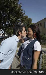 Side profile of a young man kissing a young woman leaning against a chain-link fence
