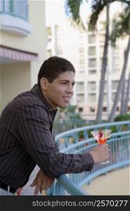 Side profile of a young man leaning against a railing and holding a cocktail