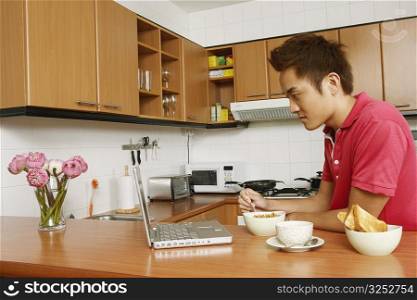 Side profile of a young man looking at a laptop at a kitchen counter