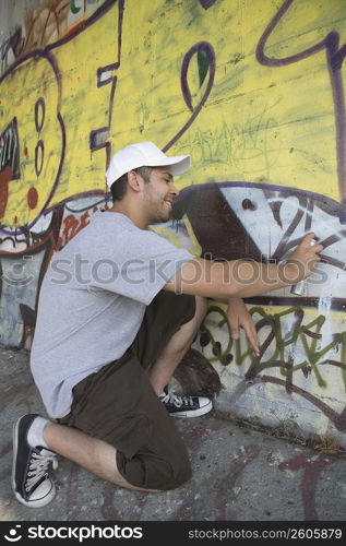 Side profile of a young man making a graffiti on a wall