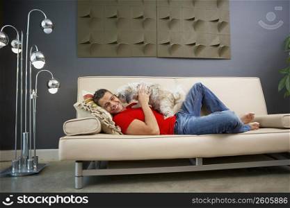 Side profile of a young man playing with his pets and lying on a couch