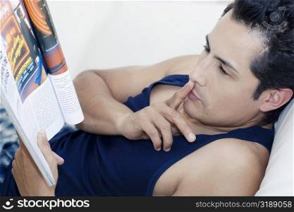 Side profile of a young man reading a magazine with his finger on his lips