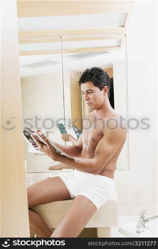 Side profile of a young man sitting in the bathroom and reading a magazine