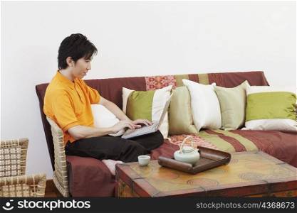 Side profile of a young man sitting on a couch and using a laptop