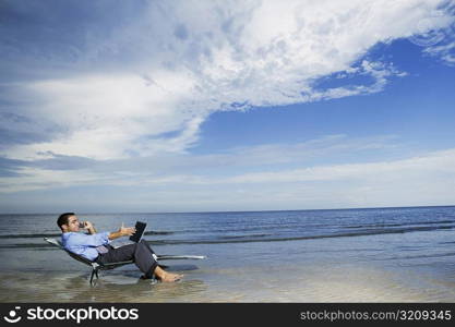 Side profile of a young man sitting on the beach with a laptop