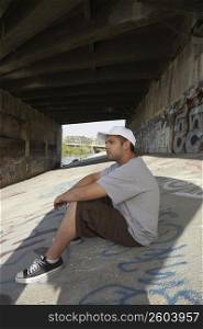Side profile of a young man sitting under a bridge