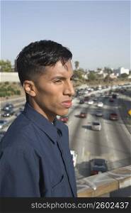 Side profile of a young man standing on an overpass and thinking