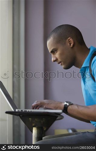 Side profile of a young man using a laptop in a cafe