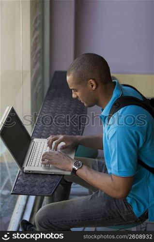 Side profile of a young man using a laptop in a cafe