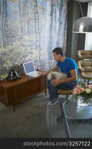 Side profile of a young man using a laptop with a dog on his lap
