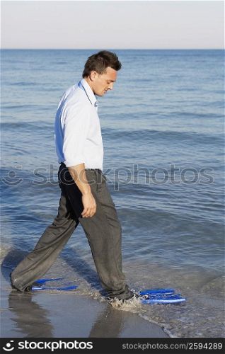Side profile of a young man wearing flippers and walking on the beach