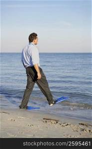 Side profile of a young man wearing flippers and walking on the beach