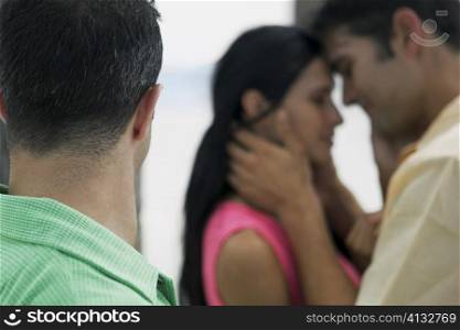 Side profile of a young man with a young woman and a mid adult man embracing each other in the background