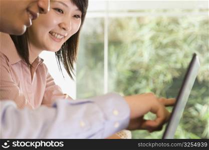 Side profile of a young man with a young woman and pointing at the screen of a laptop