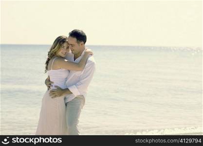 Side profile of a young woman and a mid adult man embracing each other on the beach