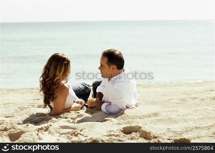 Side profile of a young woman and a mid adult man lying on the beach