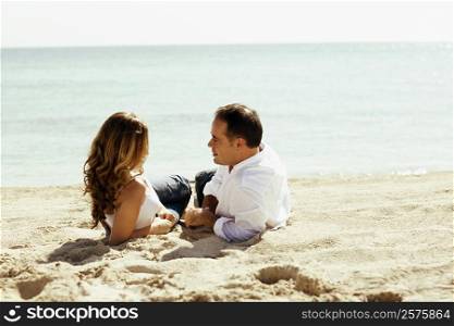 Side profile of a young woman and a mid adult man lying on the beach