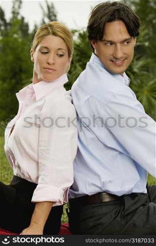Side profile of a young woman and a mid adult man sitting back to back