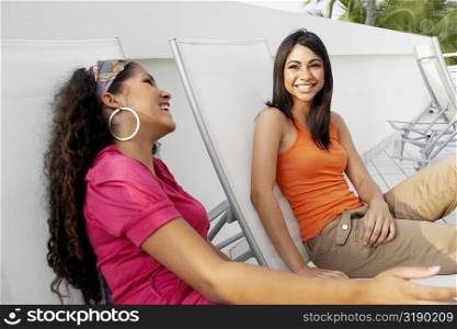 Side profile of a young woman and a teenage girl sitting on lounge chairs and smiling