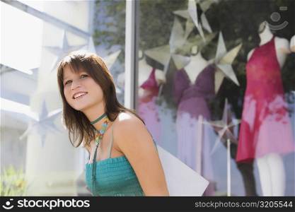 Side profile of a young woman carrying a shopping bag in front of a clothing store