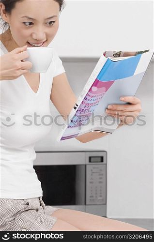 Side profile of a young woman drinking tea and reading a magazine