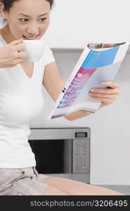 Side profile of a young woman drinking tea and reading a magazine